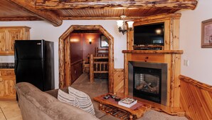 Un intérieur rustique avec un plafond en bois, un réfrigérateur noir, une cheminée et un coin salon confortable.