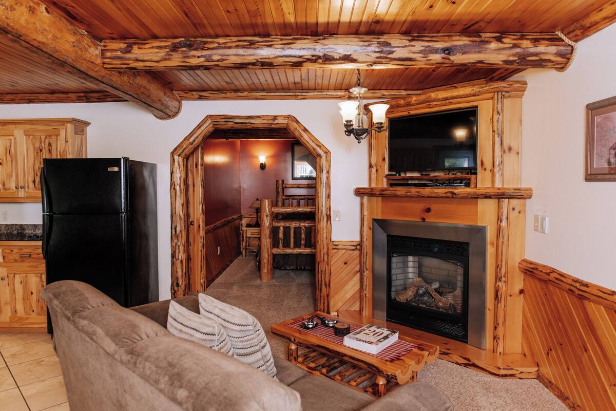 Een rustiek interieur met een houten plafond, een zwarte koelkast, een open haard en een gezellige zithoek.