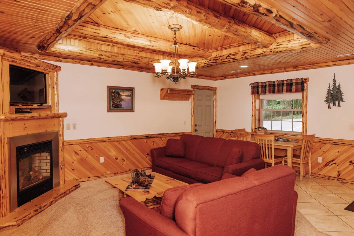 Een houten interieur met een open haard, een rode bank, een houten eettafel en een kroonluchter.