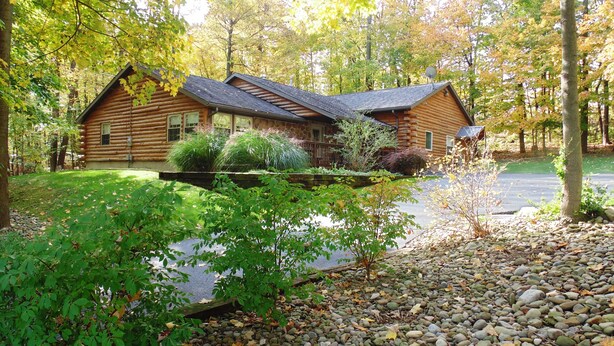Une cabane en rondins, construite sur des fondations en pierre, entourée d’un étang, et un chemin de gravier menant à l’entrée.
