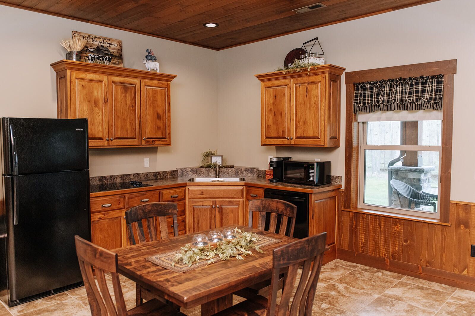 Una cocina con armarios de madera, un refrigerador negro, un microondas y una mesa de comedor con sillas.