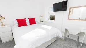 A modern bedroom with a large bed, a desk, and a TV mounted on the wall. - Seaview Cottage (Dundee)
