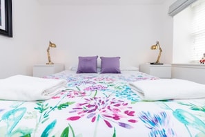 A bedroom with a bed, two bedside tables, two lamps, and a window with blinds. - Seaview Cottage (Dundee)