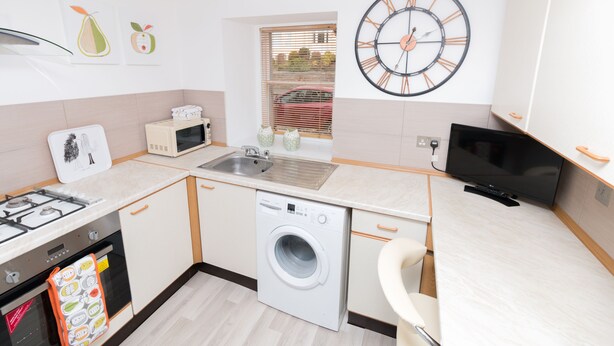 A compact kitchen with a washing machine, microwave, and sink. - Seaview Cottage (Dundee)