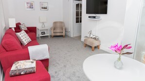 A living room with a red sofa, a beige armchair, a small white table, a TV mounted on the wall, and a vase with flowers on a white table. - Seaview Cottage (Dundee)