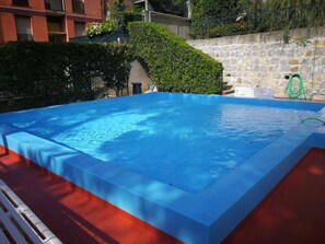 A rectangular swimming pool with a blue cover, surrounded by a stone wall and greenery. - Casa di Giò (Rapallo)