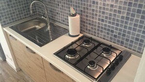 A kitchen with a stainless steel sink, a gas stove, and wooden cabinets. - Casa di Giò (Rapallo)