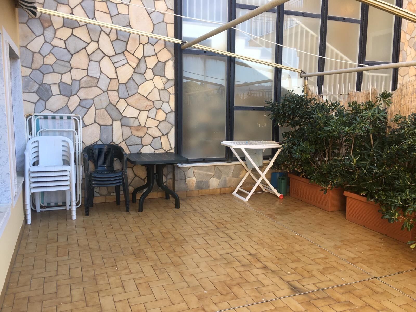 A patio area with a stone wall, a window, a folding table, two chairs, and potted plants.