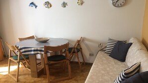 Ein Essbereich mit einem gestreiften Tisch und Stühlen, einer Uhr an der Wand und einem Sofa mit gestreiften Kissen.