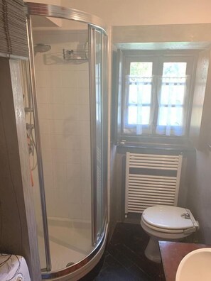 Une salle de bain avec une douche en verre, des toilettes et une fenêtre avec des stores.