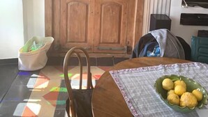 Ein Zimmer mit Holztür, einem an der Wand befestigten Fernseher, einem Tisch mit Zitronenschale und einem Stuhl.