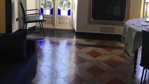 Ein Zimmer mit einem sechseckigen Fliesenboden, einem schwarzen Stuhl, einem Tisch mit grüner Tischdecke und einem Kamin mit dekorativem Sims.