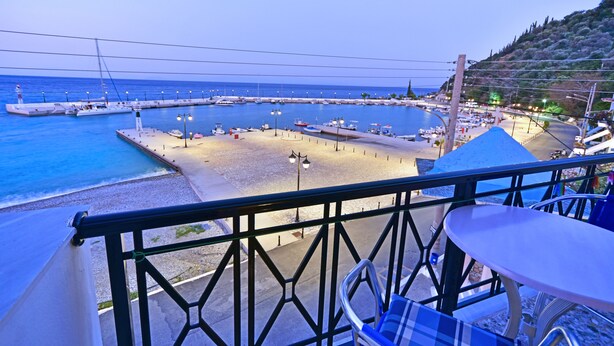 Une vue sur la mer depuis un balcon agrémenté d’une table et d’une chaise, donnant sur une marina avec des bateaux et une plage.