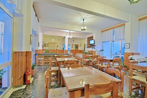 A spacious restaurant with wooden tables and chairs, a ceiling fan, and a television screen. - Hotel Blue Sea (South Kynouria)