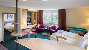 Habitación de hotel con cama, escritorio, silla, televisor, estantería y ventana con cortinas.