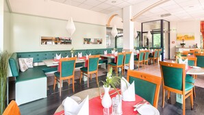 Un restaurante con asientos tapizados en verde, mesas de madera con servilletas blancas y una alfombra roja.