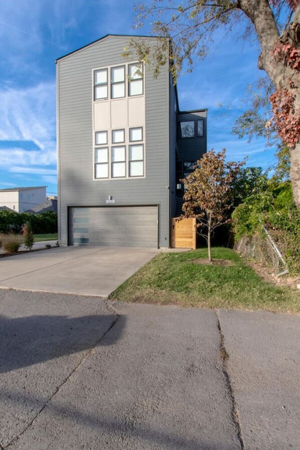 Um edifício moderno de dois andares com uma porta de garagem, uma pequena árvore no jardim da frente e um céu claro.