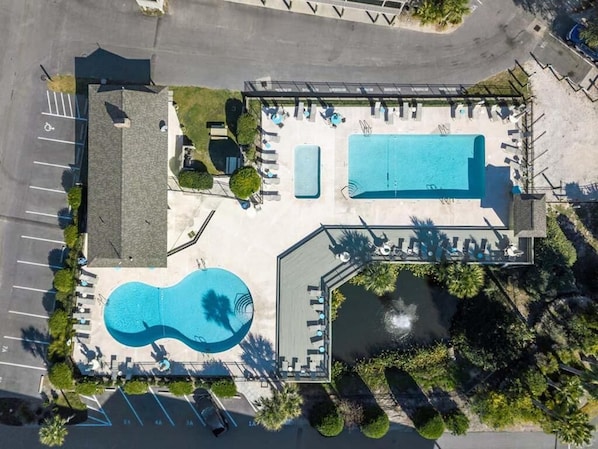 An aerial view of a resort with a large swimming pool, a smaller pool, and a hot tub area.