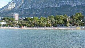 A coastal view with a beach, palm trees, and a mountain in the background. - SPACIOUS APARTMENT NEAR THE BEACH WIFI, A/C  (Dénia)