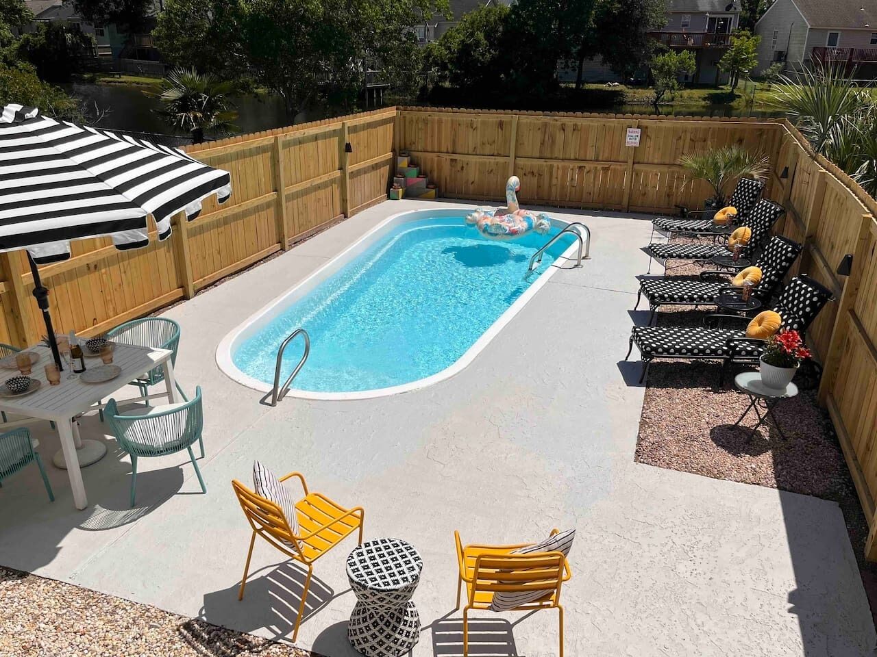 A backyard with a swimming pool, lounge chairs, and a table with chairs.