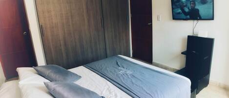 Un dormitorio con cama, armario y televisor en la pared.