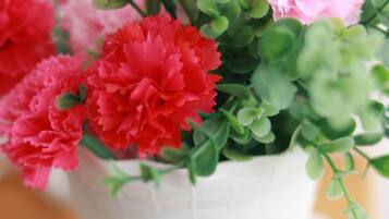 Una maceta de cerámica blanca con asa, llena de flores rosadas y rojas y follaje verde.