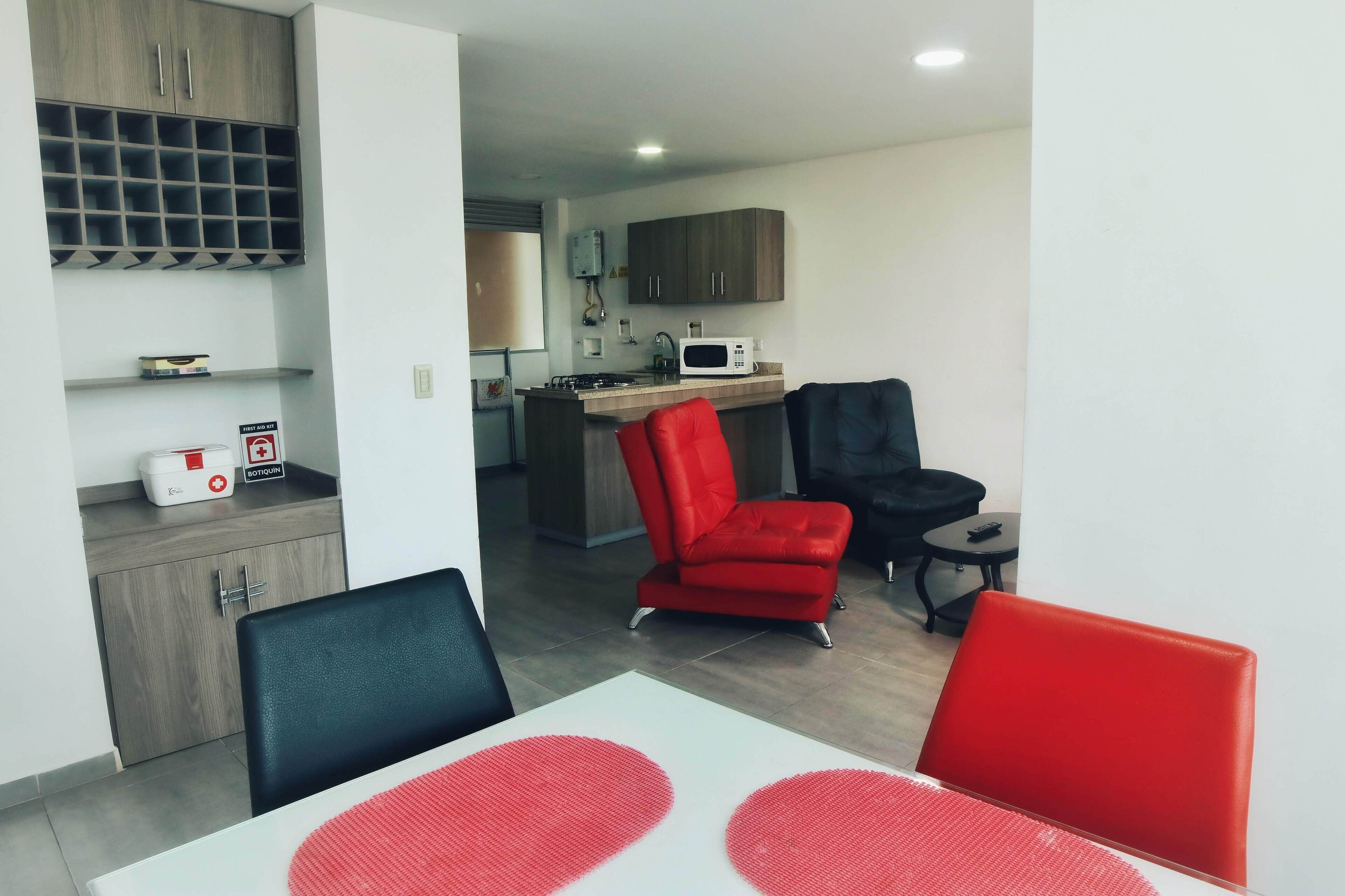 A modern kitchen with a microwave, stove, and cabinets. There are two red chairs and a black chair at a dining table with a white tablecloth.