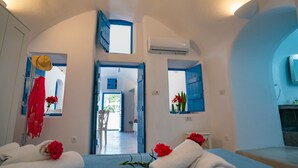 A hotel room with a bed, two windows with blue shutters, a mirror, and a red towel with flowers.