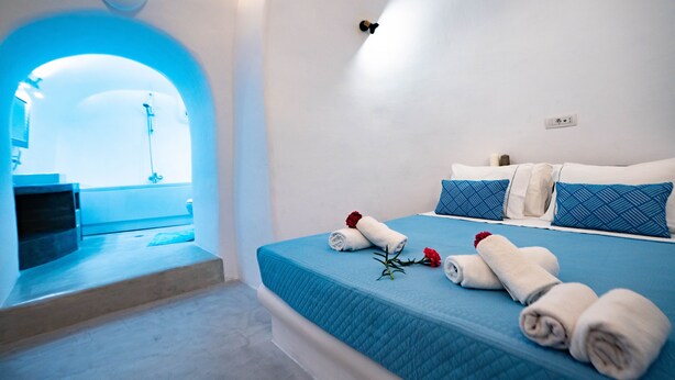 A hotel room with a bed, towels, and a view through an archway.