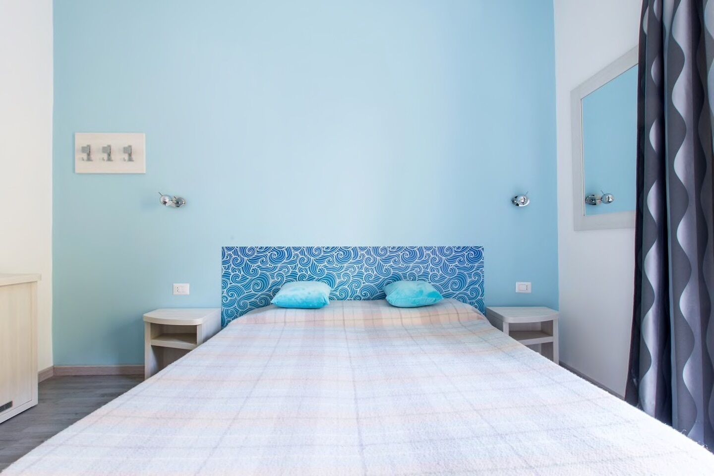 A bedroom with a bed, two bedside tables, a headboard with a wave pattern, and a mirror on the wall.