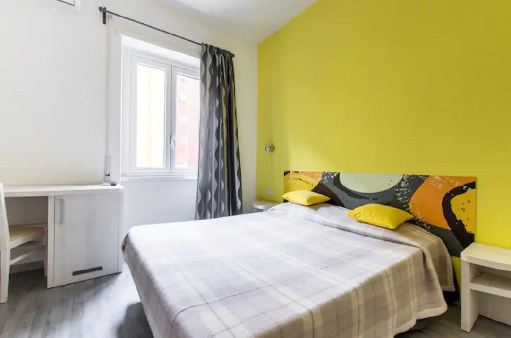 A room with a bed, a desk, and a window with curtains.