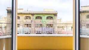 A balcony with a yellow wall and a view of a building with a green facade and arched windows. - B&B di Paolo S. (Rome)