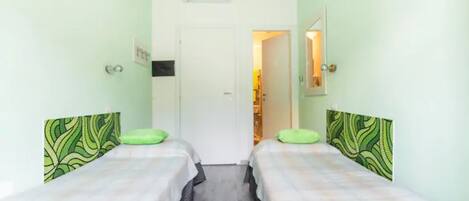 A room with two beds, a door leading to another room, and a wall-mounted air conditioner.