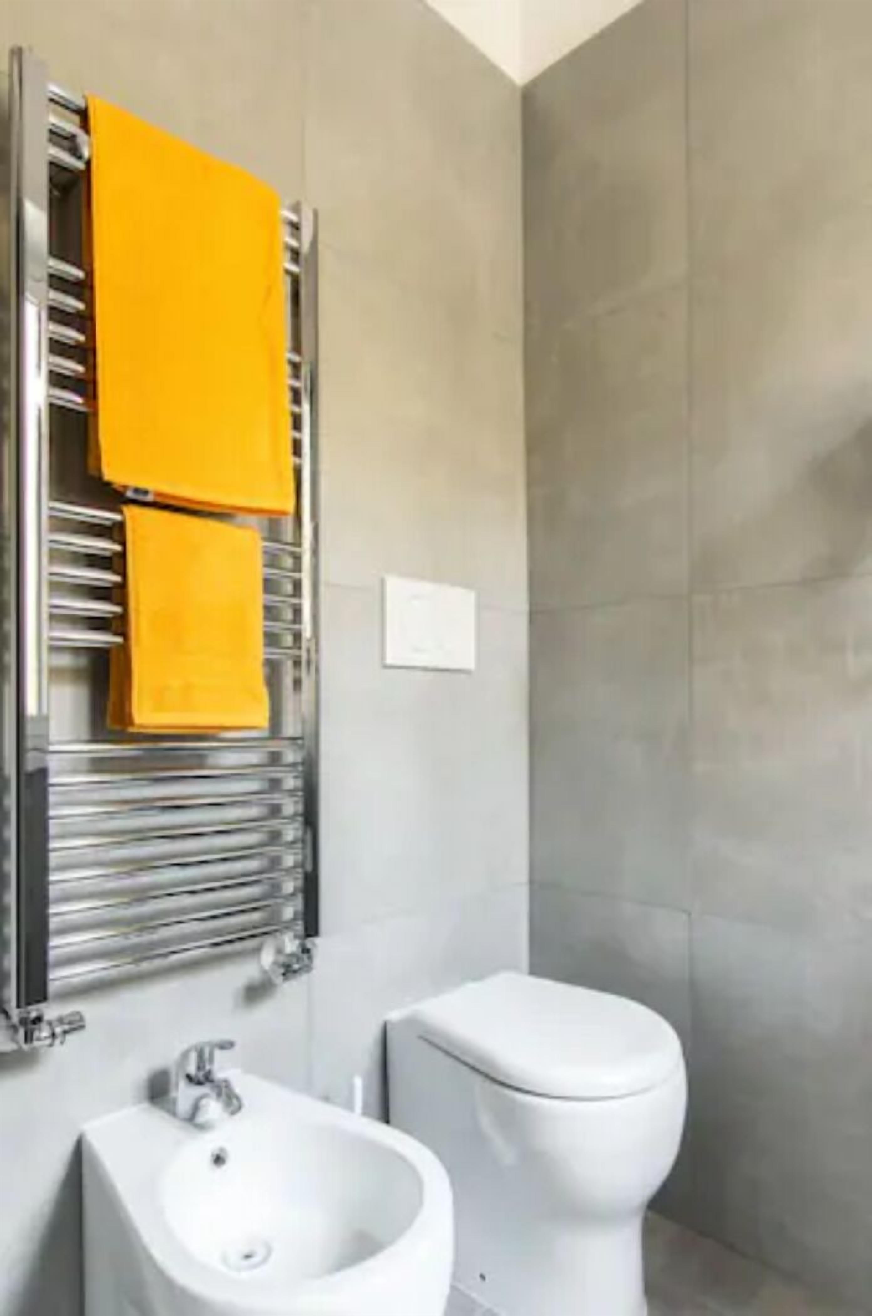 A bathroom with a white sink, a toilet, and a towel warmer with yellow towels.