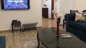 Una sala de estar con un televisor de pantalla plana, una mesa de centro con un florero, un sofá y una mesita con una computadora portátil.
