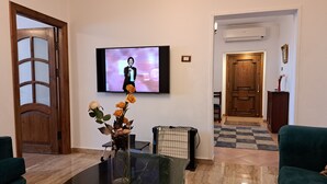 Una sala de estar con una mesa de centro de mármol, un jarrón con flores, un televisor montado en la pared y una puerta de madera.