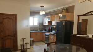 Una cocina con armarios de madera, un refrigerador negro, una mesa de comedor con sillas y una lámpara colgante.