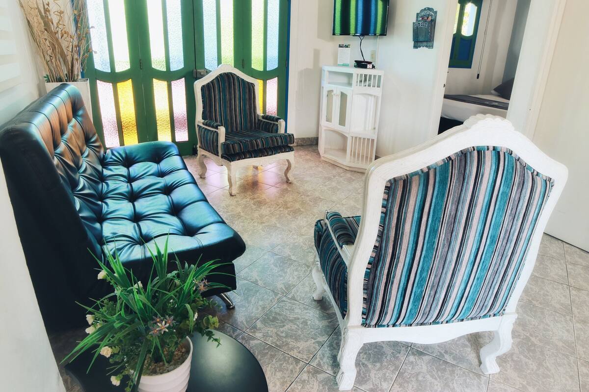 Una sala de estar con un sofá de cuero negro, un sillón a rayas y un sillón blanco. Hay una planta en maceta en la esquina.