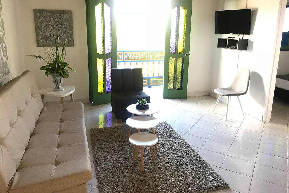 Una sala de estar con un sofá, una mesa de centro, un televisor y una puerta verde con paneles de vidrio decorativos.