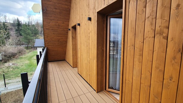 Un balcone in legno con una porta vetrata e vista su una zona boschiva.