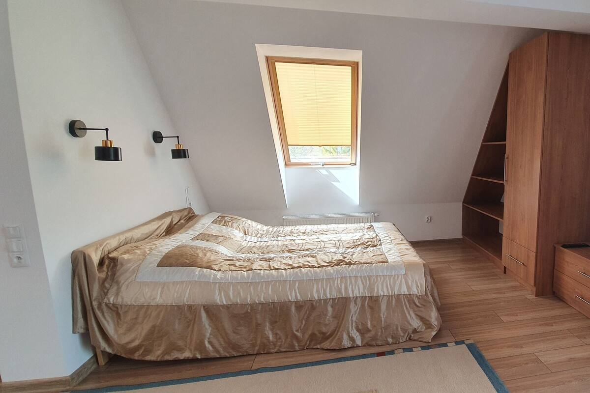 A bedroom with a bed, a TV, a wooden wardrobe, a window, and a ceiling light fixture.