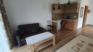 Un soggiorno moderno con un divano, un tavolino da caffè e un angolo cucina con pensili in legno e luci a sospensione.