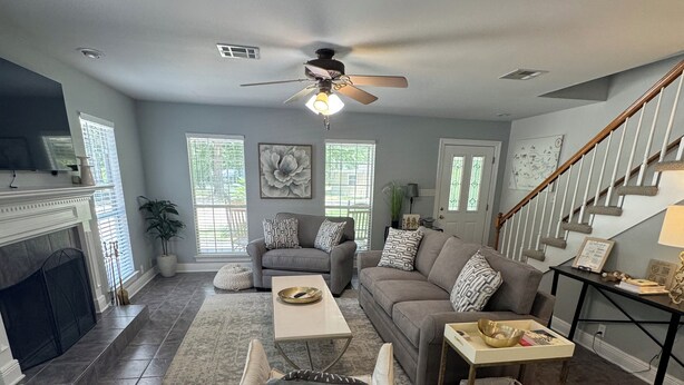 A spacious living room with a fireplace, a ceiling fan, and a staircase.