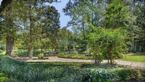 A serene garden with various trees, a wooden bridge, and a pond.