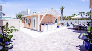A rooftop patio with a pool, outdoor seating, and a small building with a white exterior and blue accents. - A Few Steps to the Beach, at this Hidden Gem in Panama City Beach Fl. Unit-6 (Panama City Beach)