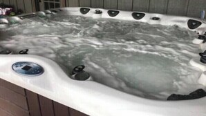 Un jacuzzi con múltiples chorros, un panel de control y una terraza de madera que lo rodea.