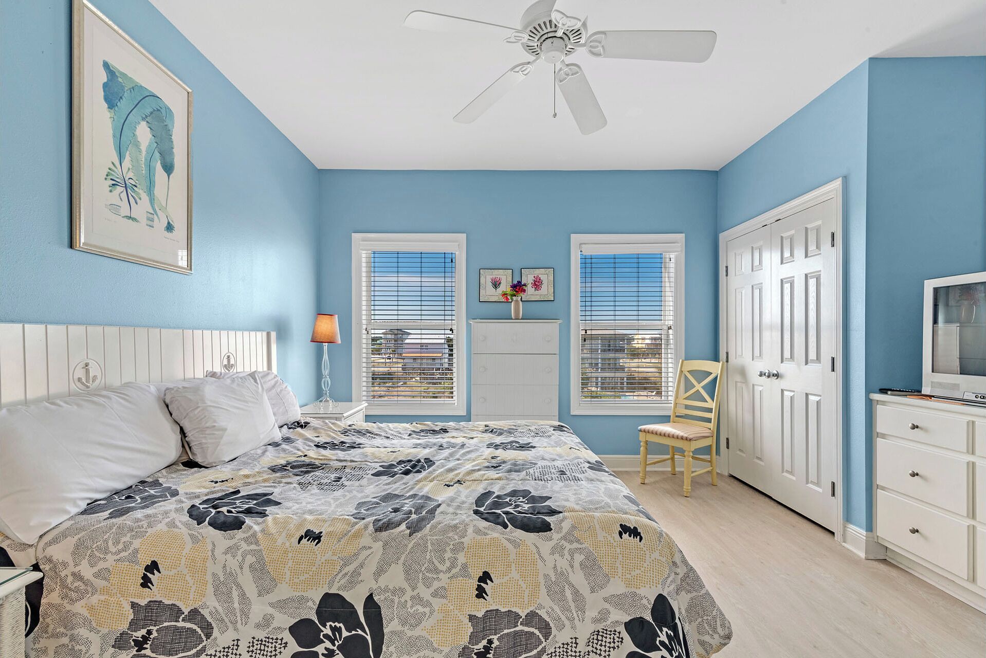 Une chambre à coucher comprenant un lit, un ventilateur de plafond, une chaise, une commode et un téléviseur.