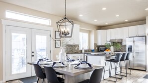 Une cuisine moderne avec des meubles blancs, un réfrigérateur en acier inoxydable et un coin repas comprenant une table en bois et des chaises noires.