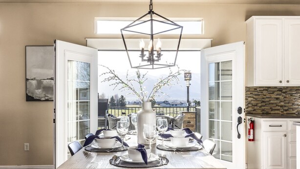 Un coin repas avec une table dressée pour quatre personnes, un lustre et une vue sur l’extérieur.