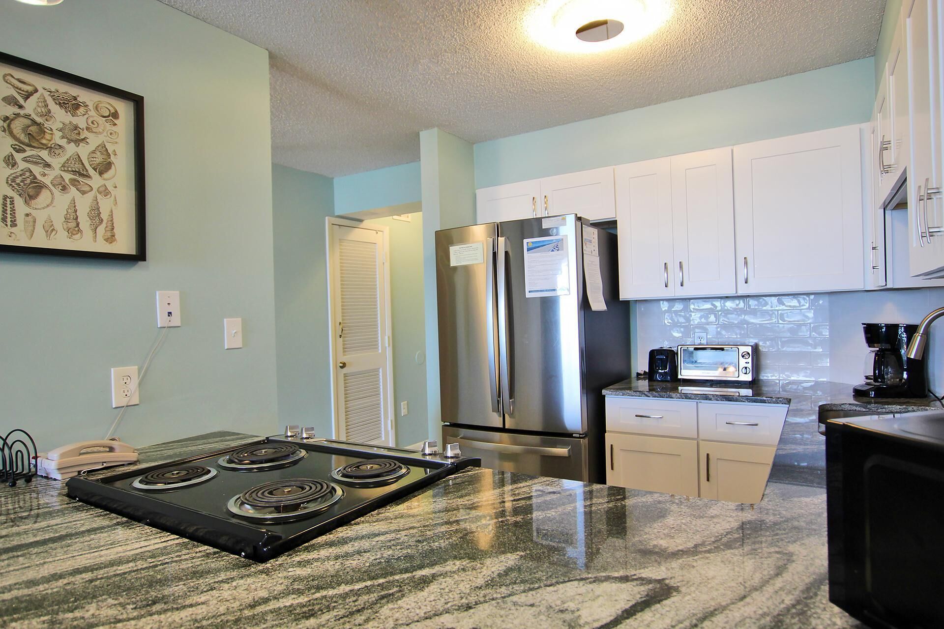 A compact kitchen with white cabinets, a stainless steel refrigerator, a microwave, and a stove.